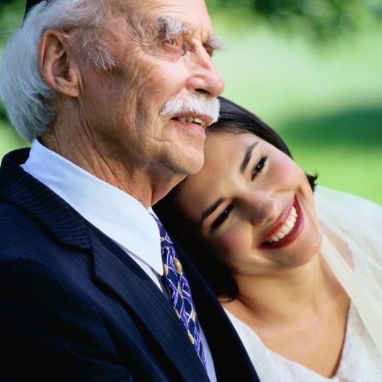 Bride resting her head
on her grandfather's shoulder. Both are smiling.