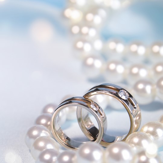 A String of pearls with two platinum
wedding rings, each set with one diamond,
on a blue background