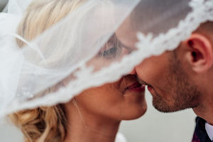 White bride and groom kissing under bridal
veil