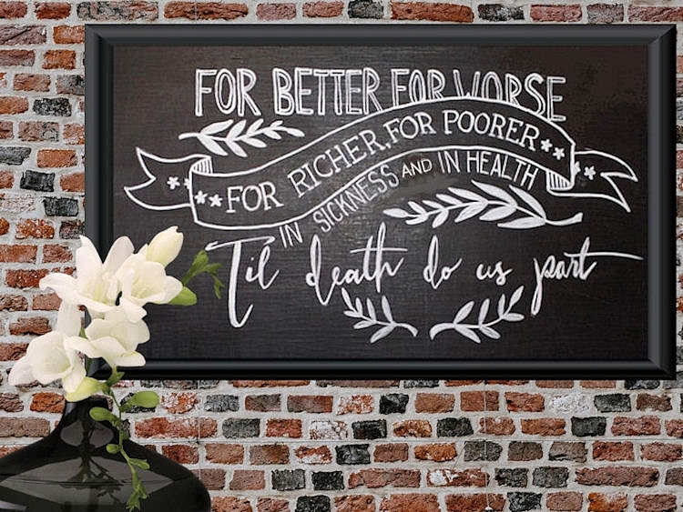 Chalkboard with the
traditional wedding vows hanging on a brick wall
with a black vase of white flowers in front of it